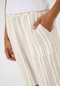 Shorts légers rayés en crème et beige avec une taille élastique et des poches latérales. Le tissu a une finition douce et texturée.