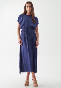 Navy blue maxi dress with gathered waist, short sleeves, and relaxed fit made of lightweight fabric. Paired with beige block-heel sandals.