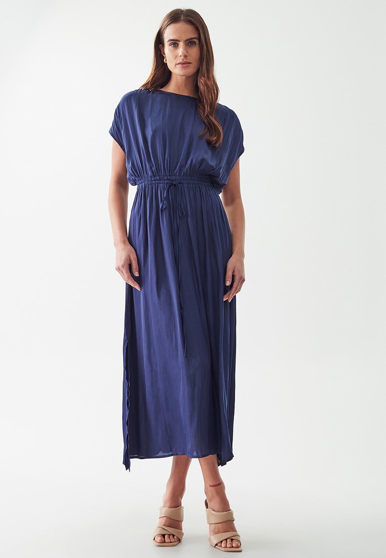 Navy blue maxi dress with gathered waist, short sleeves, and relaxed fit made of lightweight fabric. Paired with beige block-heel sandals.