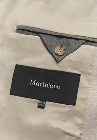 Beige fabric with a black tag reading "Matinique," featuring a gray button and a gray lining at the pocket. Size label EUR 50, USA 40.