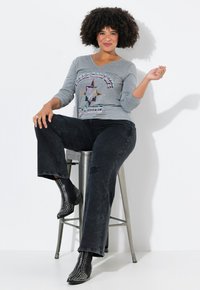 T-shirt gris à col en V et manches longues avec un design graphique d'étoiles, associé à un jean noir évasé. Bottines noires avec des accents cloutés.