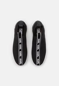 Svarta stickade slip-on sneakers med en vit sula. Har en upprepande textetikett "KARL" i vitt på framsidan och en stadig dragflik bak.