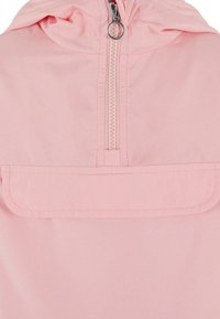 Lys rosa vindjakke med hette, halv glidelås foran og en frontlomme. Glatt stoff med sømmer og detaljer i sølvfarge.