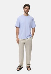 Světle fialové tričko s kulatým výstřihem a volným střihem, spárované s béžovými oblekovými kalhotami. Modelka nosí černé sandály s dvojitým popruhem.