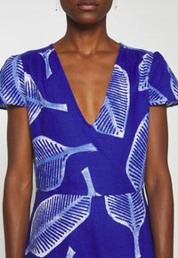 Blå klänning med djup V-ringning, korta ärmar och ett bladmönster i vitt och ljusblått över tyget.