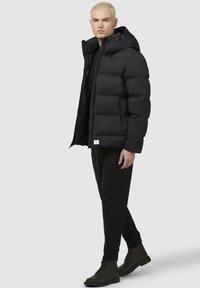 Fekete steppelt dzseki kapucnival, cipzáros záródással és oldalsó zsebekkel. Fényes anyagból készült; dobozos szabású és rugalmas mandzsettákkal rendelkezik.