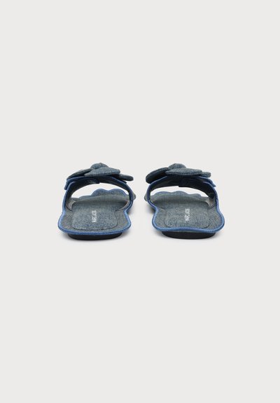 Paire de chaussons bleus à bout ouvert, bords festonnés et grandes fleurs en tissu sur le dessus, vues de face sur fond uni.