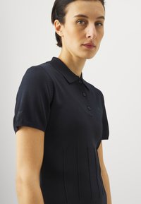 Námořnická polo košile s přiléhavým designem, krátkými rukávy, třemi knoflíky a vertikálními žebrovými detaily na přední straně.
