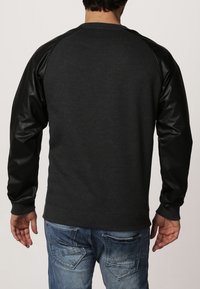 Sudadera gris oscuro con mangas de cuero negro, puños y dobladillo de canalé, que presenta un corte relajado y un diseño de mangas raglán. Vista trasera mostrada.