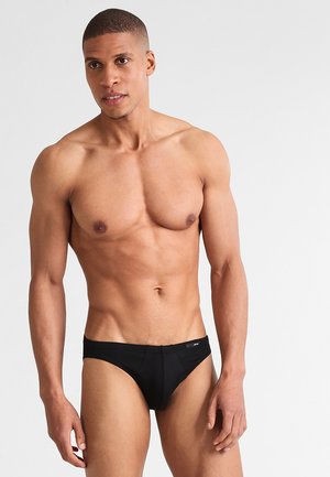 Schwarze Bikiniunterwäsche aus glattem Stoff, mit einem niedrigen Schnitt, minimaler Naht und einem kleinen Logosticker am Bund.