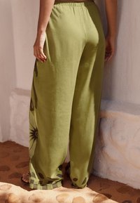 Grønne hørbukser med brede ben og botanisk print i mørkegrøn på siderne. Elastisk talje, afslappet design og flydende tekstur.