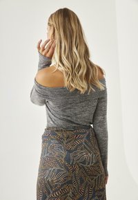 Top gris sin mangas con hombros al descubierto y mangas largas, combinado con una falda azul con un patrón que presenta diseños en hojas doradas y moradas. Textura suave.