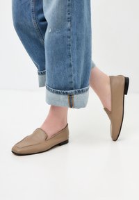 Pantofi slip-on din piele bej, cu o textură netedă și un design rotunjit. Toc mic negru. Purtați cu blugi ușor blue denim, cu tiv.