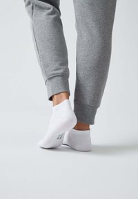 Weiße Knöchelsocken, die zusammen mit grauen Sweatpants präsentiert werden. Die Socken haben gerippte Bündchen und eine glatte Textur. Die Sweatpants haben elastische Bündchen.