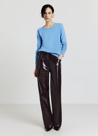 Helles blaues Strickpullover mit runder Halslinie, kombiniert mit glänzenden, dunkelbordeauxfarbenen Hosen mit weitem Bein, die Fronttaschen und eine glatte Textur aufweisen.