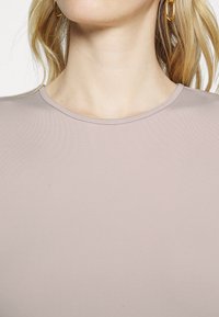 Ljus mauve figurnära topp med rund halsringning; tillverkad av ribbat tyg, slät textur och utan synliga mönster eller detaljer i metall.