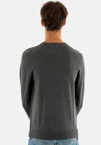 Pull en maille gris avec un col rond, des manches longues et des poignets côtelés. Texture lisse ; porté avec un jean bleu clair.