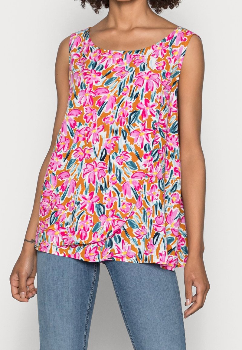 Haut sans manches à motif floral avec des fleurs roses et oranges porté avec un jean bleu clair, montré des épaules jusqu'aux hanches sur une femme.