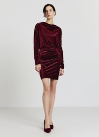 Bordeauxrotes Samtkleid mit langen Ärmeln, drapiertem Ausschnitt und seitlichen Raffungen. Kombiniert mit passenden bordeauxroten High Heels.
