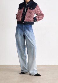 Chaqueta de mezclilla recortada con estampado rojo y marino, combinada con jeans de pierna ancha azul claro y zapatos negros de punta. Se puede ver el material texturizado.