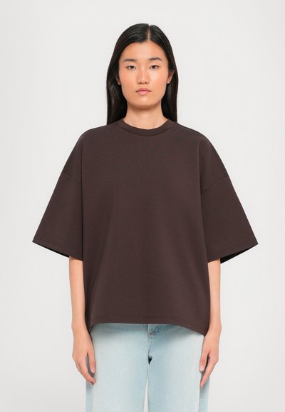 T-shirt marron surdimensionné à manches courtes, col rond, en tissu lisse, associé à un jean en denim bleu clair.
