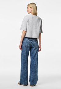 Sivi obrezan pulover s kratkimi rokavi, v kombinaciji z modrimi širokimi jeans hlačami z zadnjimi žepi in izbledelim učinkom. Brez opaznih vzorcev.