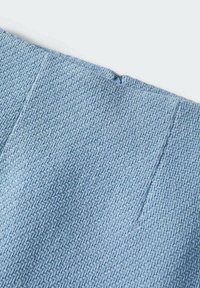 Gros plan d’un tissu bleu clair texturé avec un motif tissé et une petite fermeture éclair invisible partiellement visible sur le bord supérieur.