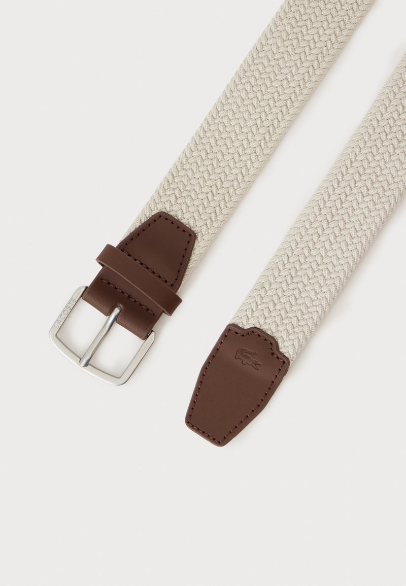 Beige woven fabric belt with brown leather buckle and tip, featuring a silver metal buckle and embossed crocodile logo on the leather tip.