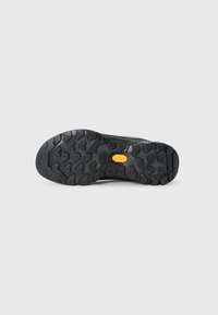Sorte robuste turstøvlesåle med dype mønstre og en gul Vibram-logo i midten på en ensfarget lys bakgrunn.
