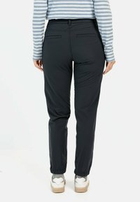 Sorte, lette bukser med elastisk talje og manchetter. To baglommer. Matchet med en grå langærmet stribet skjorte og hvide sneakers.