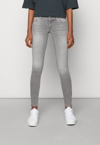 Jeans ajustados grises con un ligero desgaste, que presentan una cintura de altura media y un dobladillo desgastado, combinados con zapatillas blancas para un look casual.