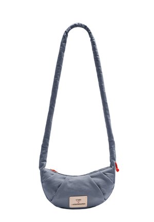 Small crescent-shaped gray shoulder bag with padded strap and red zipper pull, featuring a rectangular white brand label on front.