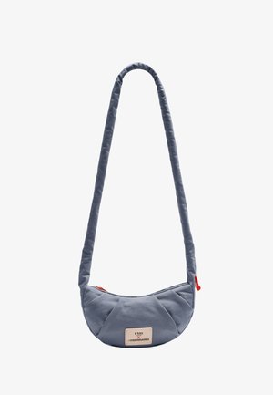 Kleine, halbmondförmige graue Schultertasche mit gepolstertem Riemen und rotem Reißverschlussanhänger, vorne mit einem rechteckigen weißen Markenetikett.