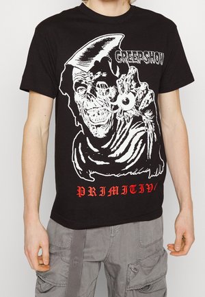 Camiseta de algodón negra con un estampado gráfico de una figura de calavera, texto rojo que dice "PRIMITIV" y detalles en blanco. Manga corta, cuello redondo.