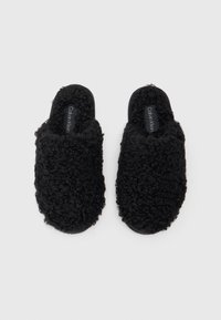 Fekete papucs, amely textúrált anyaggal van borítva, puha, bolyhos felülettel. Slip-on dizájnnal és lapos talppal rendelkezik. A logó látható a bélésen.