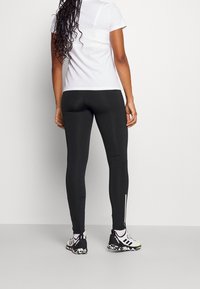 Leggings neri realizzati in tessuto elastico, con una vestibilità slim, design senza cuciture e dettagli riflettenti bianchi sulla parte inferiore della gamba.