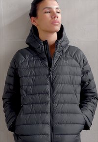 Dunkelgraue Pufferjacke mit Reißverschluss, Kapuze, gestepptem Design und genähten Details. Geeignet für kaltes Wetter.