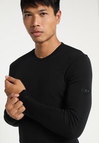 Czarna longsleeve z miękkiego materiału, z okrągłym dekoltem i dyskretnym logo na lewym rękawie. Dopasowany krój i gładka tekstura.