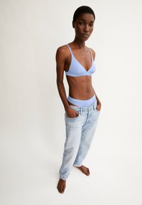 Light blue, triangular bralette with thin straps paired with loose, faded blue jeans, featuring front pockets and a relaxed fit.