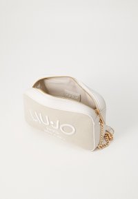 Clutch in tessuto beige con dettagli in pelle bianca, tracolla in catena dorata, chiusura con zip e logo in rilievo sulla parte frontale. Interno di colore chiaro.