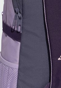 Lila och grå ryggsäck med texturerad tyg, dubbla dragkedjor, sidficka i nät och en kontrasterande logotypdetalj.