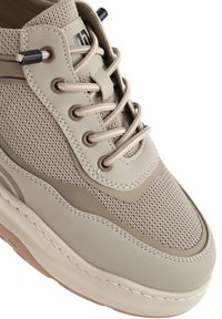 Zapatillas beige con parte superior de malla y acentos de cuero liso, cordones redondos y suela texturizada con un diseño en capas.