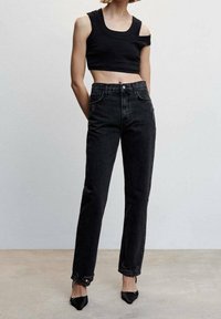 Top negro recortado y jeans negros de cintura alta. Los jeans tienen pierna recta y un sutil detalle desgastado en el dobladillo. Zapatos negros de punta afilada.