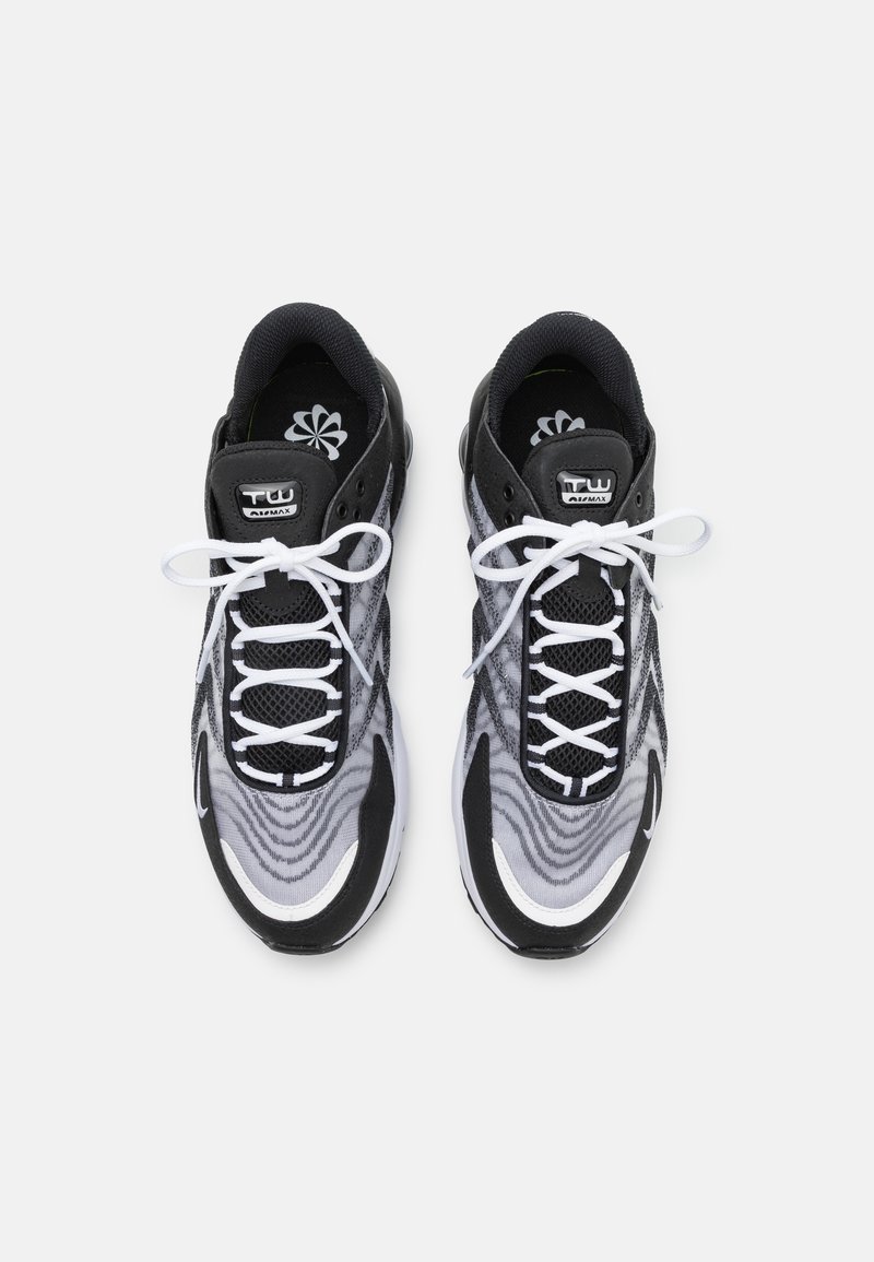 Zapatillas deportivas en blanco y negro con parte superior de malla, patrón ondulado y cordones blancos en contraste. Presentan un collar acolchado y un logo en la lengüeta.