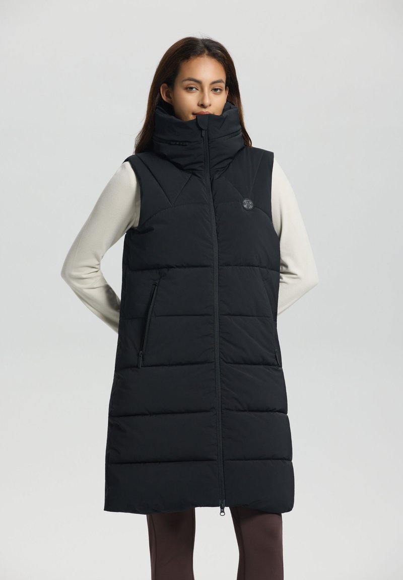 Gilet de survêtement noir avec col haut, couture horizontale, poches latérales zippées et fermeture éclair à l'avant. Petit logo sur la poitrine.