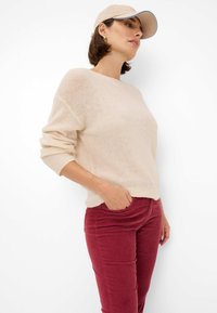 Pull en tricot nude à coupe décontractée, avec des manches longues. Assorti à un pantalon en velours côtelé rouge, mettant en valeur le contraste de textures et de couleurs.
