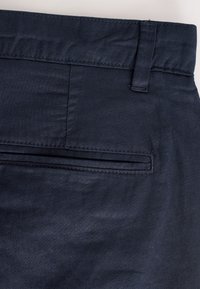 Meresinise tekstuuriga lamedad riidest püksid, millel on sirge lõige, vööaasad ja üks tagatasku korraliku õmblusega.