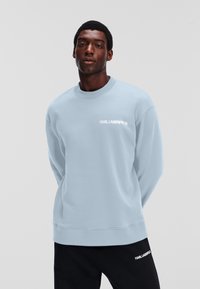 Svetlo modra pulover s krožnim izrezom in dolgimi rokavi, z belim logotipom "KARL LAGERFELD" na prsih. Mehka tkanina, sproščen kroj.