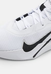 Hvid sportssko med struktureret overdel, som har en sort Nike swoosh, hvide snørebånd og et glat såledesign. Accenter inkluderer subtile mønstre.