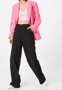 Rosa kavaj över en rosa crop top, matchad med svarta rutiga vida byxor och vita sneakers. Kavajen har en avslappnad passform och slag.